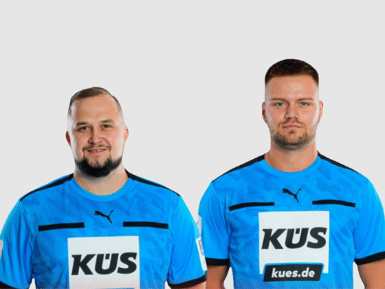 Zwei männliche Fußballspieler stehen in blauen Puma-Trikots mit KÜS und kues.de auf der Vorderseite nebeneinander und posieren vor einem schlichten hellgrauen Hintergrund, als wären sie bereit für ein Foto mit einem Schiedsrichter Handball.