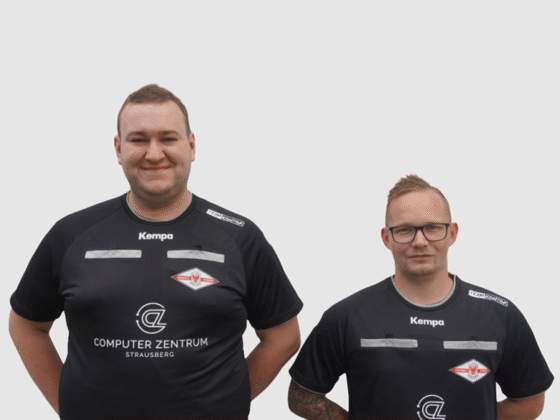 Zwei Männer in schwarzen Hemden stehen zusammen und sehen aus wie Schiedsrichter, die sich auf ein Spiel vorbereiten.