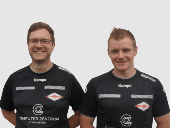 Zwei Männer stehen nebeneinander, beide lächeln und tragen passende schwarze Sporttrikots mit weißen Logos und Texten, darunter Kempa, Computer Zentrum Strausberg und Schiedsrichter Handball, vor einem schlichten hellen Hintergrund.