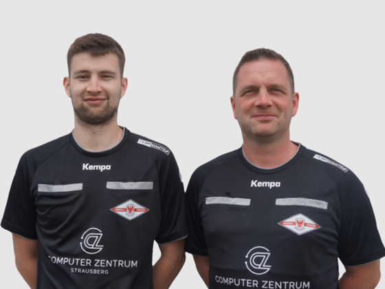 Zwei Männer in schwarzen Sporttrikots mit den Logos von Computer Zentrum Strausberg und Kempa stehen nebeneinander vor einem schlichten weißen Hintergrund. Die beiden Schiedsrichter Handball schauen in die Kamera und lächeln leicht.