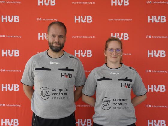 Zwei Personen in grauen Sportshirts stehen vor einem roten Hintergrund mit der Aufschrift „HVB“ und Logos. Beide tragen eine Brille, blicken in die Kamera und lächeln leicht. Auf den Shirts steht „Computerzentrum Strausberg“.