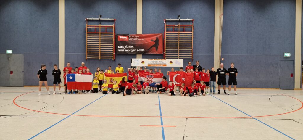 Eine große Gruppe von Kindern und Trainern posiert während der Mini-WM in einer Sporthalle und hält dabei die Flaggen von Chile, Spanien, Kroatien und der Türkei in den Händen.