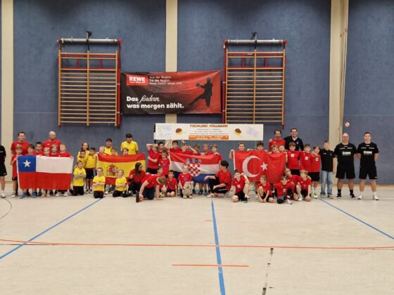 Eine große Gruppe von Kindern und Trainern posiert während der Mini-WM in einer Sporthalle und hält dabei die Flaggen von Chile, Spanien, Kroatien und der Türkei in den Händen.
