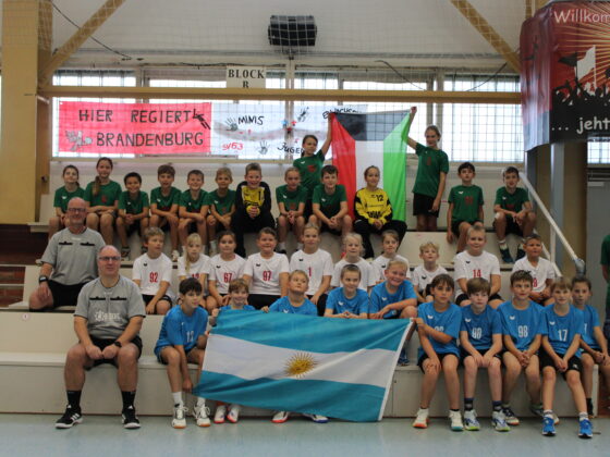 Eine große Gruppe junger Handballspieler und -trainer posiert beim HVB-Pokal-Final-Four 2026/27 auf den Tribünen der Halle mit palästinensischen und argentinischen Flaggen.